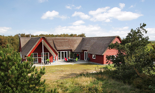 Blick auf ein rotes, reetgedecktes Gruppenferienhaus auf der dänischen Nordseeinsel Rømø